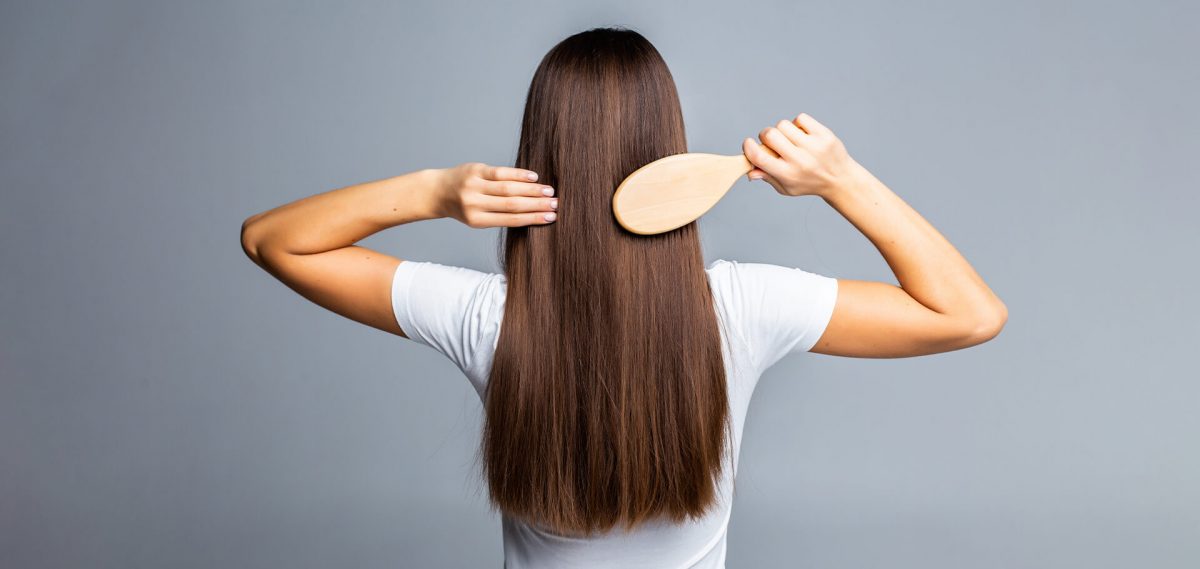 Mujer peinándose su cabello largo de espaldas